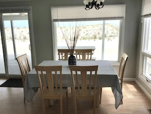 A dining area with a table and chairs, a vase with reeds, and a view of a desert landscape through large windows. - Pet friendly beachfront vacation rental on LBI (Brant Beach)