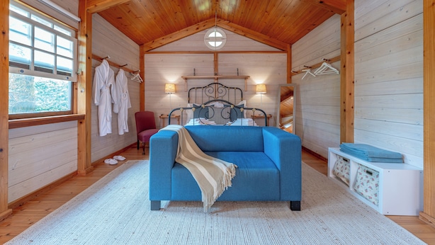 A cozy room with a blue sofa, wooden walls, a bed with a headboard, and a window with clothes hanging on a rack. - Azores Green Villas (Ponta Delgada)