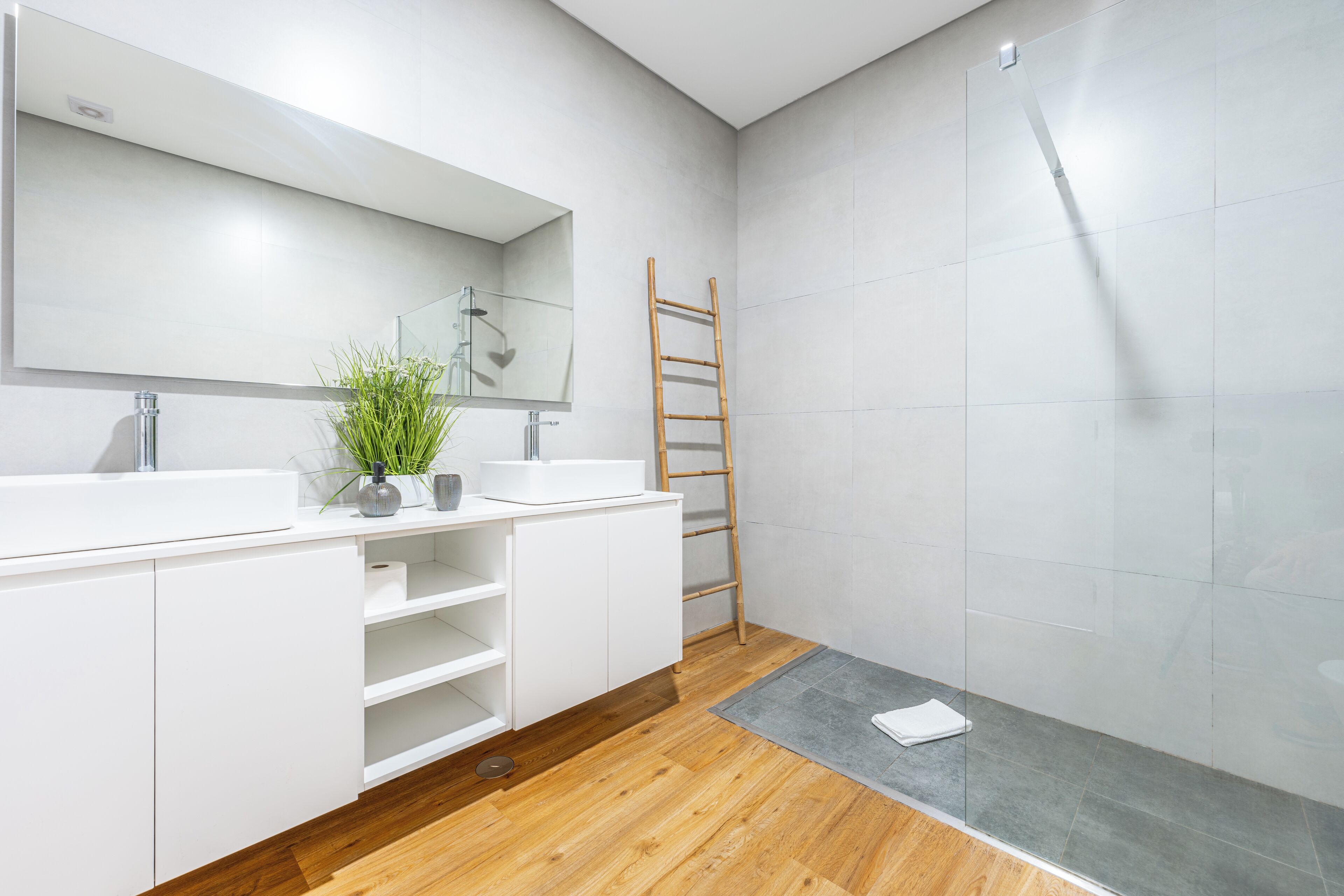 A modern bathroom with two sinks, a large mirror, a shower, and a wooden ladder.