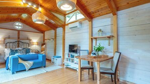 A cozy cabin interior with a wooden ceiling, a blue sofa, a wooden dining table, and a television on a white shelf. - Azores Green Villas (Ponta Delgada)