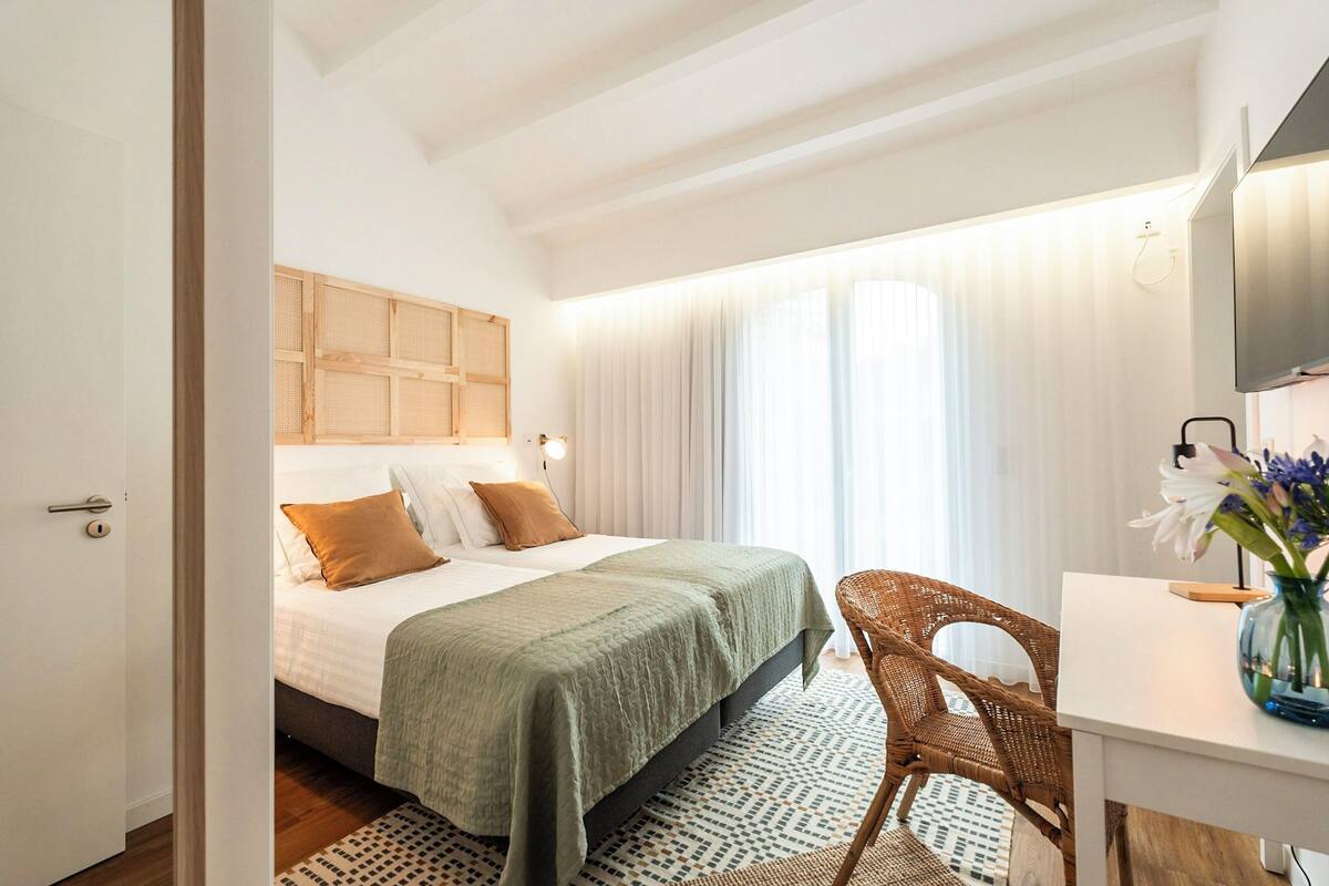 Une chambre d’hôtel avec un lit, un bureau, une chaise et une grande fenêtre avec des rideaux.