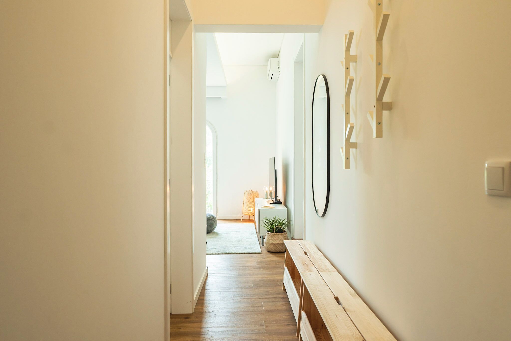 A hallway with wooden flooring, a bench, a small table with a plant, and a mirror on the wall.