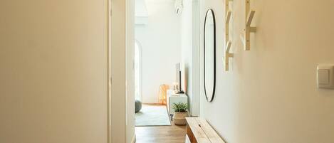 A hallway with wooden flooring, a bench, a small table with a plant, and a mirror on the wall.