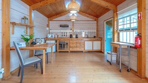 A wooden interior with a dining table, chairs, a kitchen area with cabinets and appliances, and a hanging light fixture. - Azores Green Villas (Ponta Delgada)
