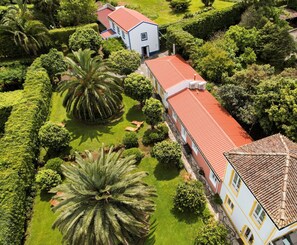 An aerial view of a property with a long building with a red roof, surrounded by well-maintained gardens and palm trees. - Azores Green Villas (Ponta Delgada)