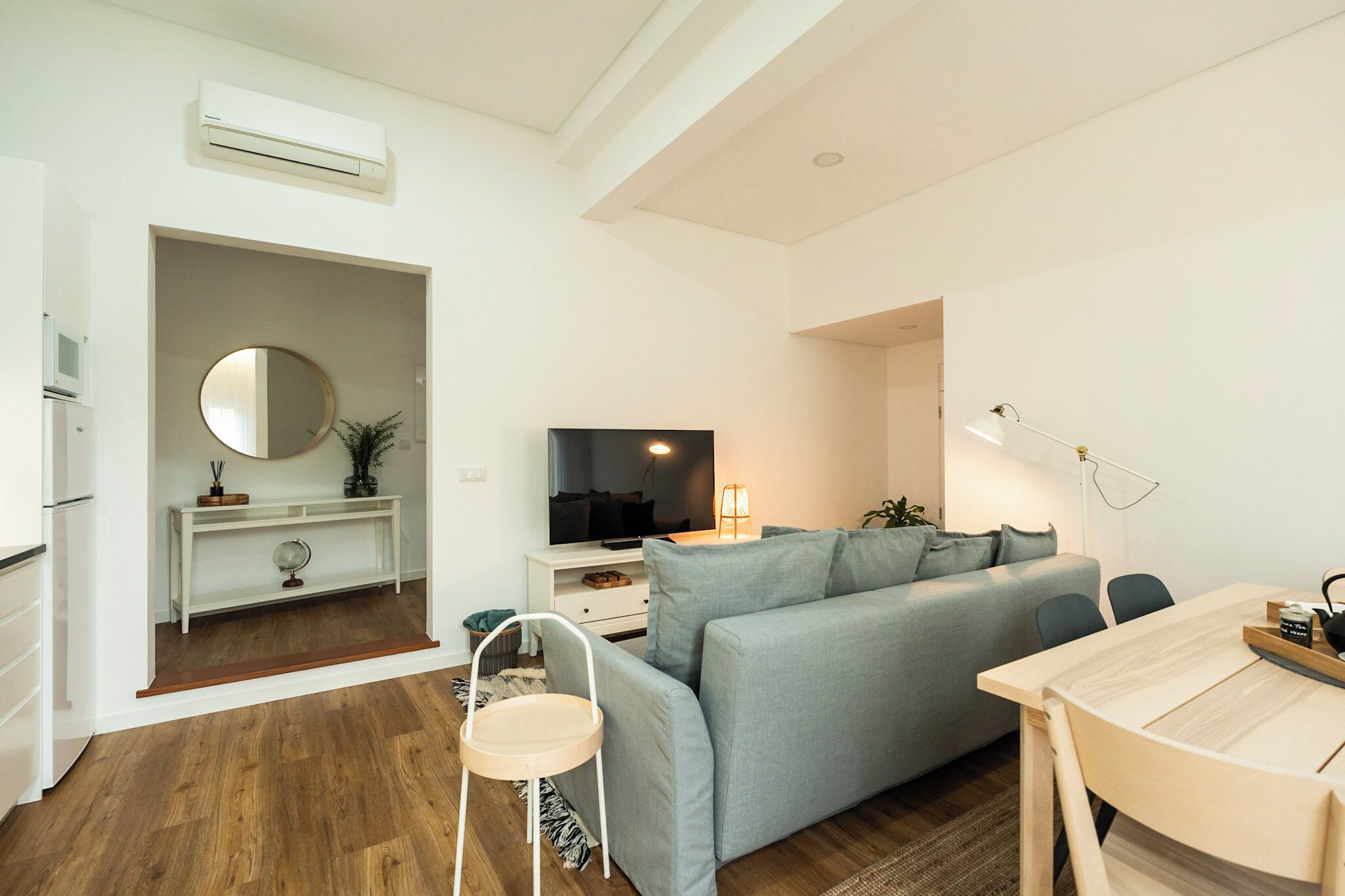 A modern living room with a grey sofa, a wooden dining table, and a TV.
