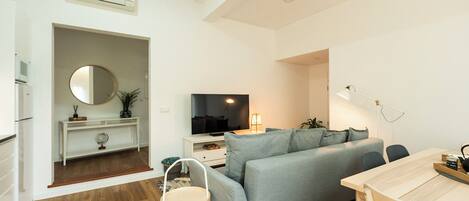 A modern living room with a grey sofa, a wooden dining table, and a TV.