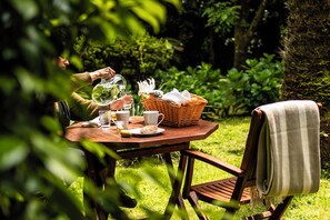 A wooden table set outdoors with a basket, cups, and a bottle. - Azores Green Villas (Ponta Delgada)