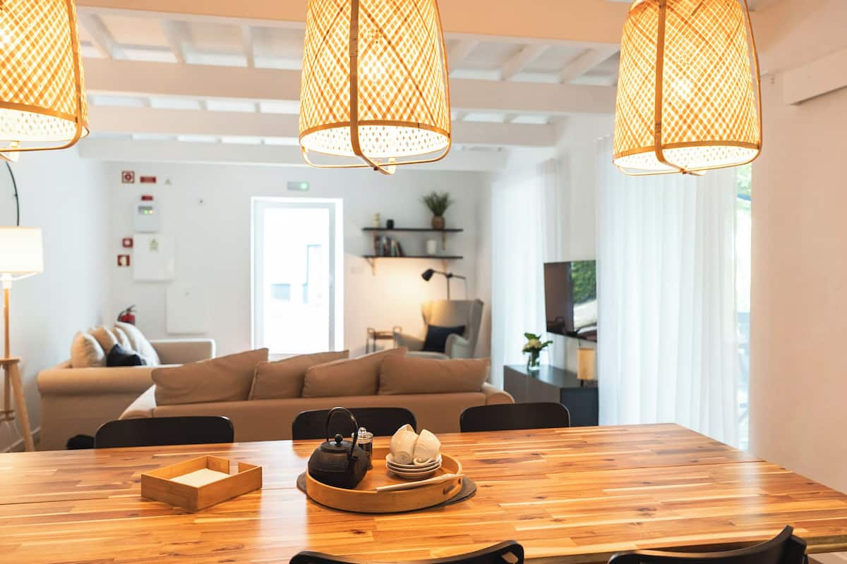 Un espace repas moderne avec une table en bois, un plateau contenant une théière et des tasses, et un canapé en arrière-plan.