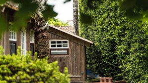 A rustic wooden cabin with a tiled roof, surrounded by lush greenery and a small patio with a table and chairs. - Azores Green Villas (Ponta Delgada)