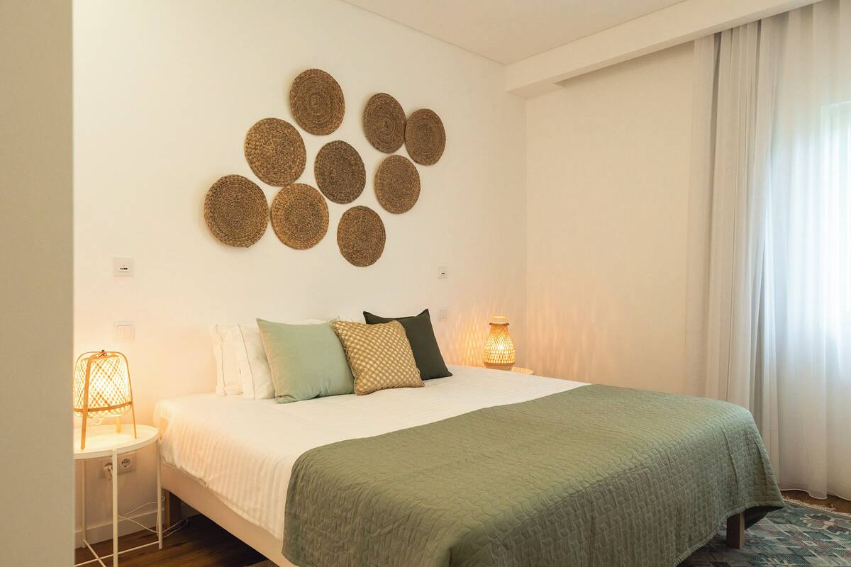 Une chambre à coucher bien rangée, avec un lit, des oreillers, un élément de décoration circulaire fixé au mur et une lampe de chevet.