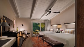 Habitación de hotel con una cama grande, un escritorio con lámpara, una silla, un banco, un ventilador de techo y vistas al exterior.