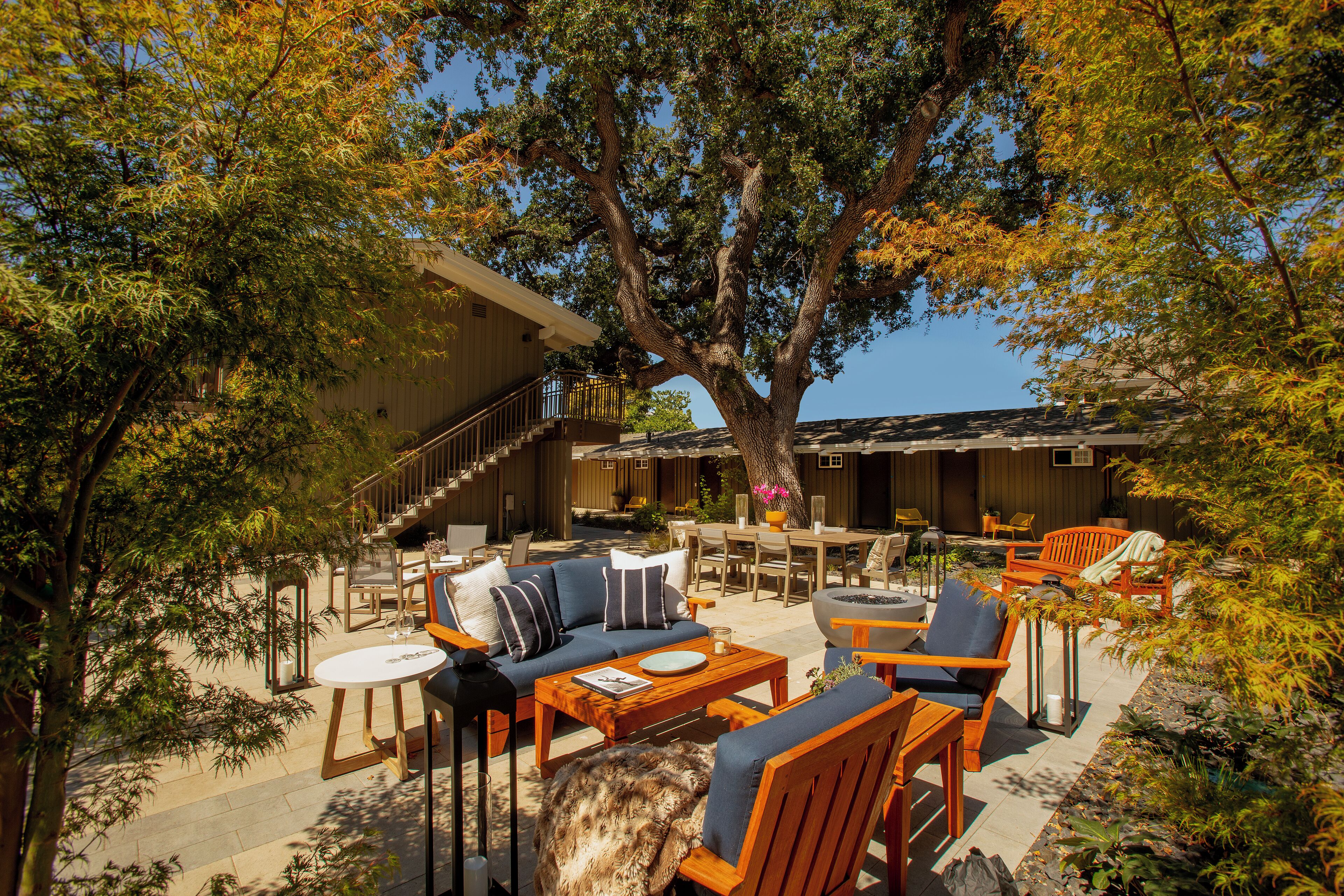 An outdoor patio with wooden furniture, a dining area, and a staircase leading to an upper level.