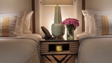 Habitación de hotel con dos camas, una mesita de noche con lámpara, un jarrón con flores y un teléfono.