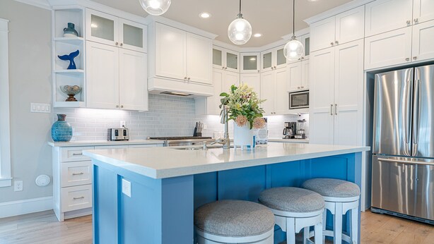 Una cocina moderna con armarios blancos, una isla central con taburetes, un refrigerador de acero inoxidable e iluminación colgante.