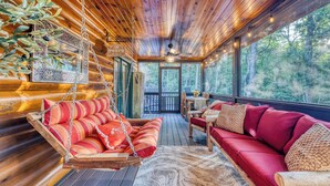Un interior de cabaña acogedor con un sillón colgante, un sofá rojo y un comedor con vistas al bosque.