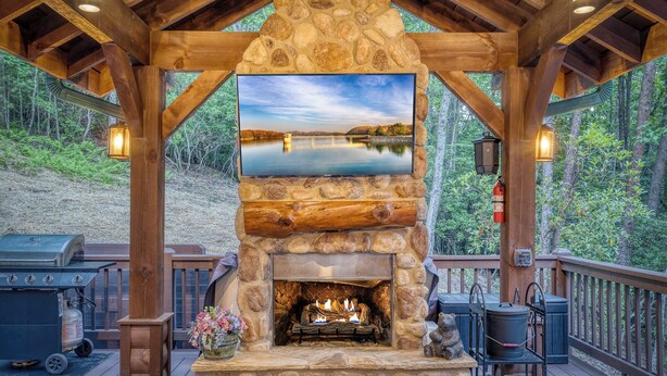 Una chimenea de piedra con fuego, un televisor montado encima y una terraza con mobiliario exterior.