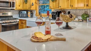 Una cocina con armarios de madera, encimera de mármol, una botella de vino fresa Barefoot, dos copas de vino, una tabla de quesos con galletas y una cesta tejida.