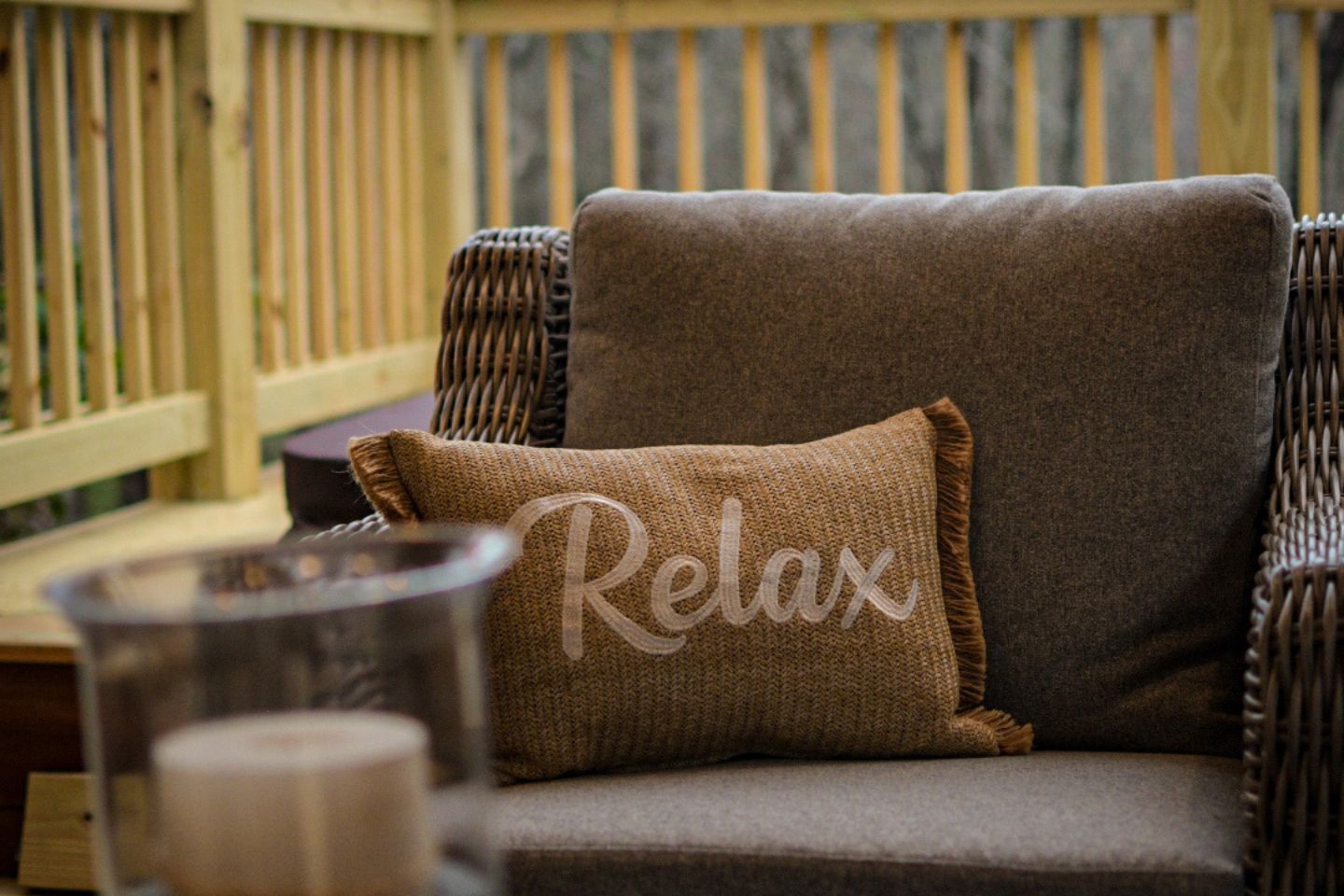 Une chaise en osier avec un coussin sur lequel est écrit « Détendez-vous » et une bougie posée sur une table.