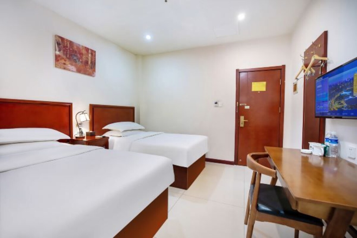 Une chambre d’hôtel avec deux lits, une table en bois, une télévision et une porte.