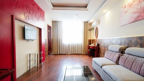 A modern living room with a sofa, a TV, and a large window with curtains. - Greentree Inn Zhengzhou Chengnan Road Bojue Hotel (Zhengzhou)