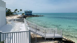 A beachside view with a wooden deck, clear turquoise water, and a blue building.