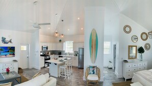 A spacious living area with a kitchen, dining area, and a bedroom with a large bed and a surfboard decoration.