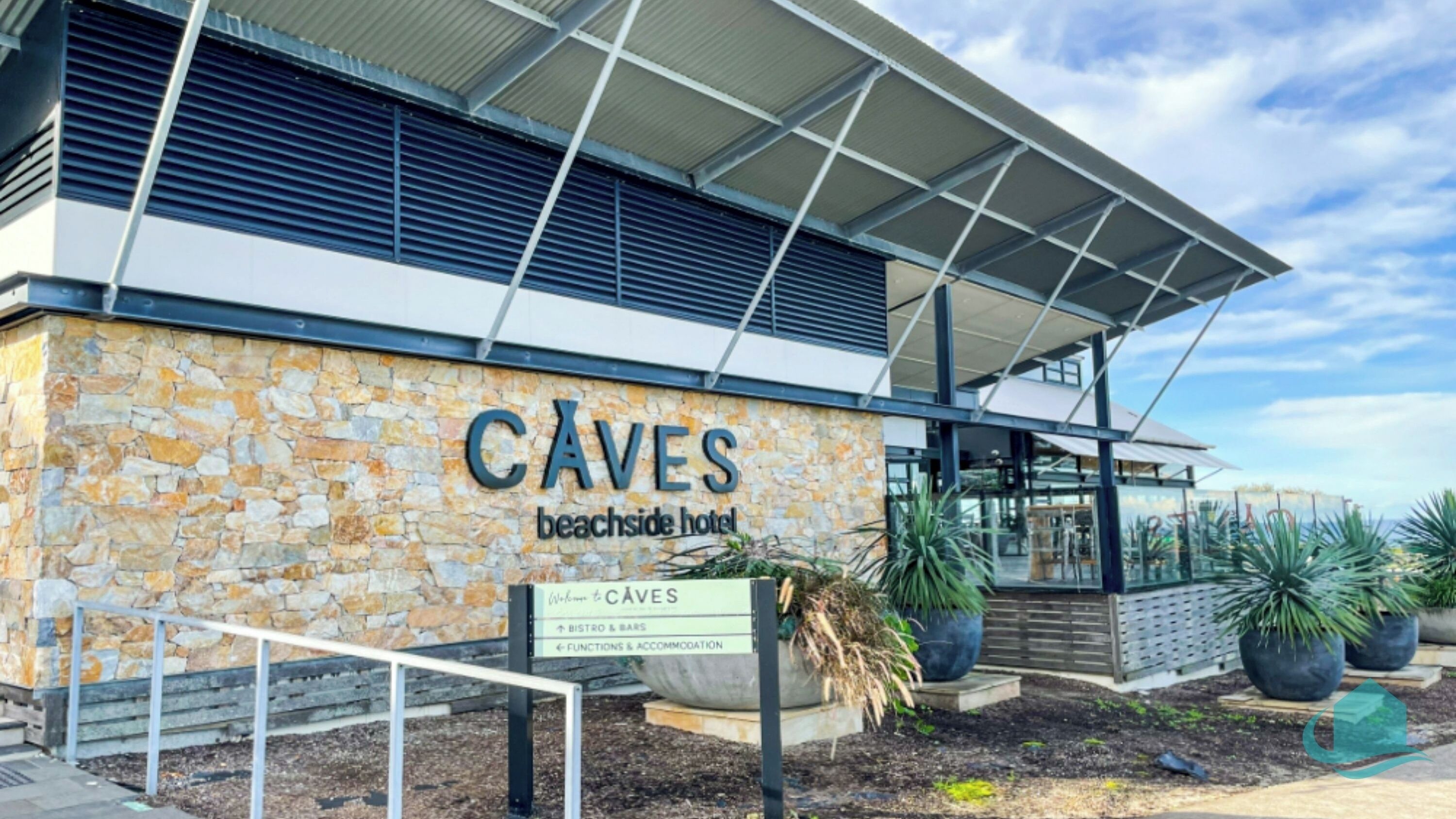 Hotellet Caves Beachside har en stilig exteriör med en fasad av sten, en modern entré med ett glastak och en skylt som visar hotellets namn och vilka bekvämligheter det erbjuder.