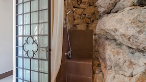 Área de chuveiro com parede de pedra e porta de vidro com moldura metálica decorativa.