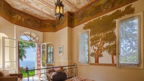 Quarto com cama, janela com mural de árvore e vista para o mar.