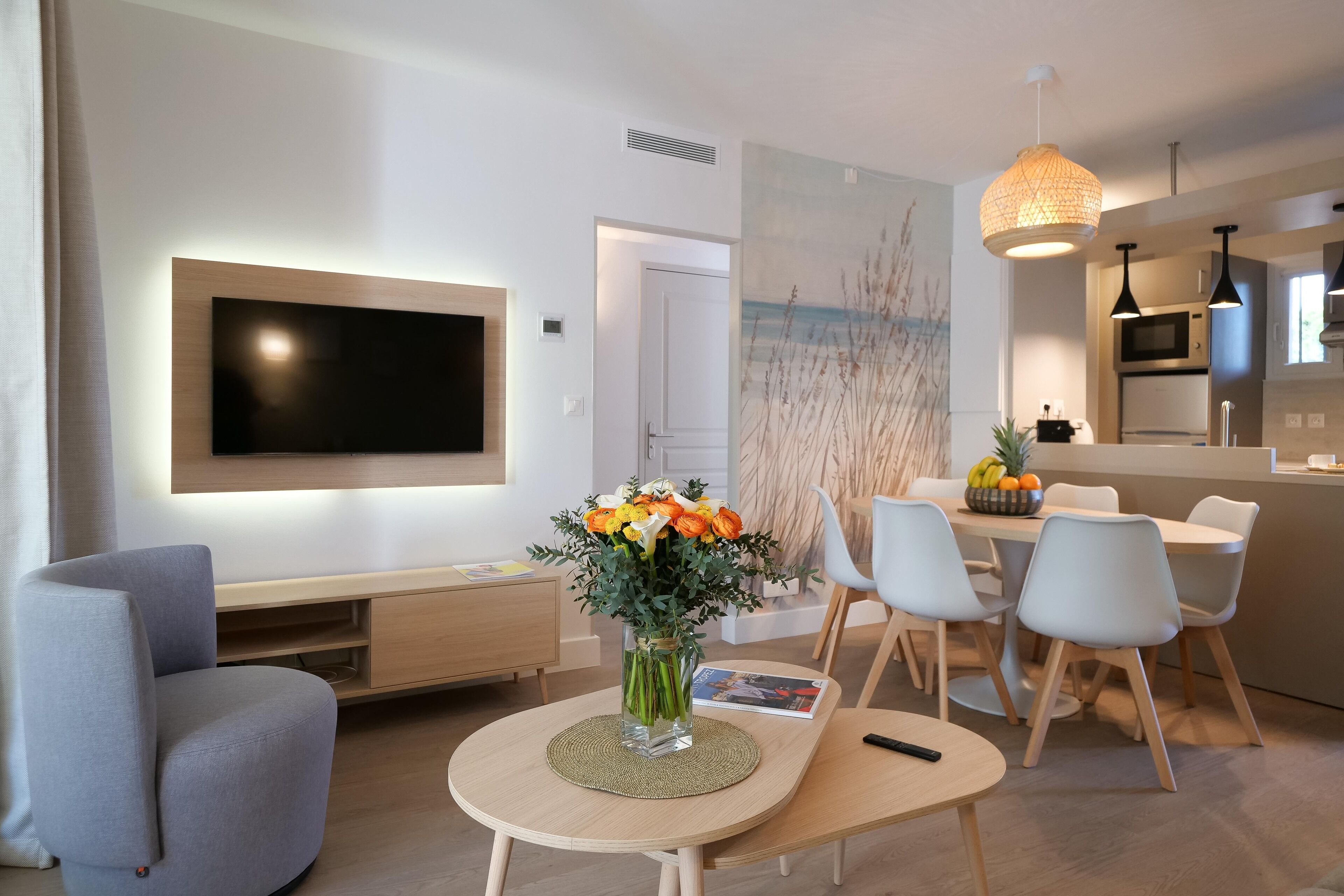 Una sala de estar moderna con un televisor de pantalla plana, un comedor con mesa y sillas, y una cocina al fondo.