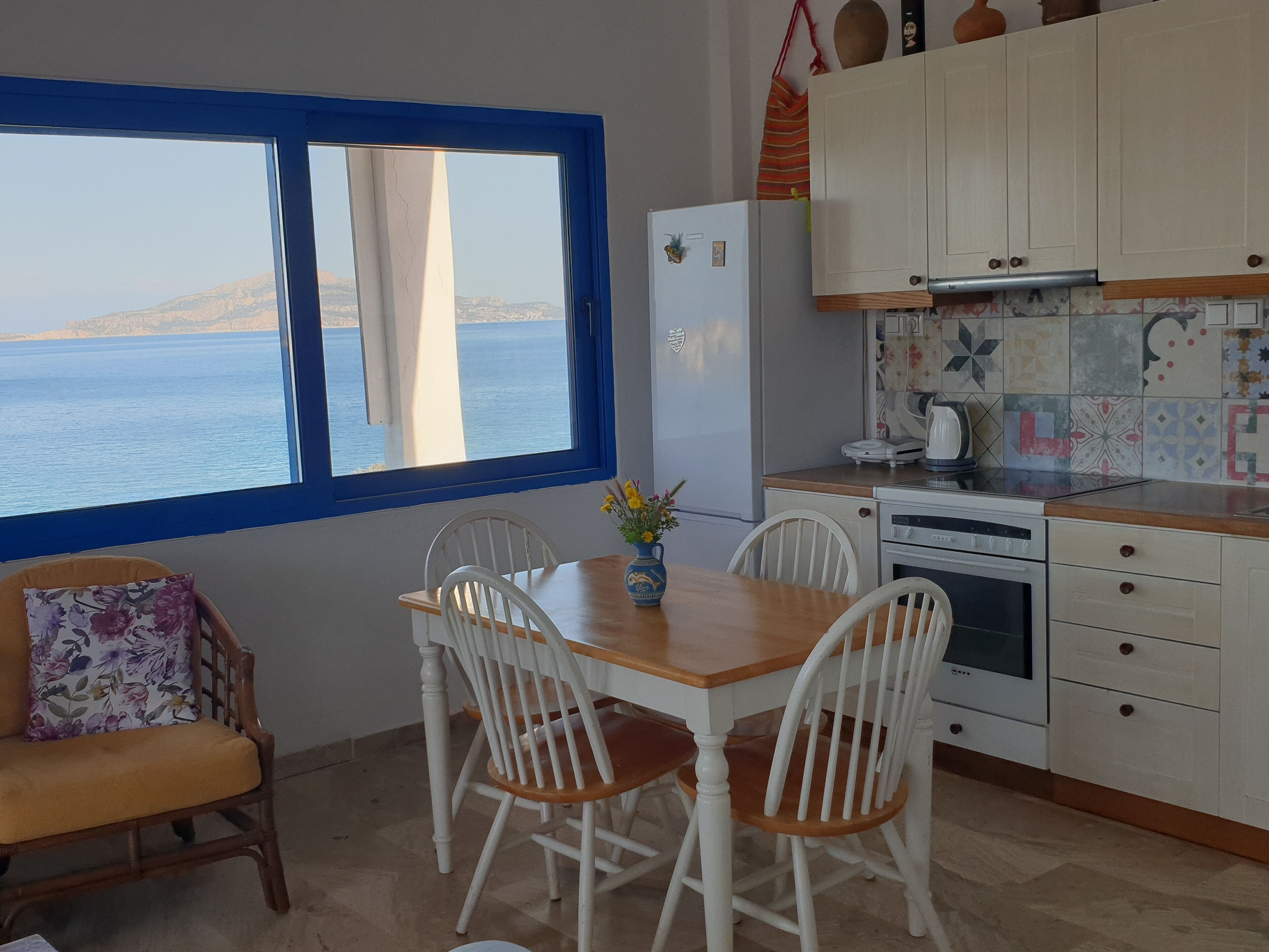 A kitchen with a view of the sea, white cabinets, a wooden table, and white chairs.