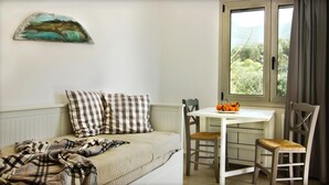 A cozy room with a bed, a table with chairs, a window with a view of greenery, and a painting on the wall.