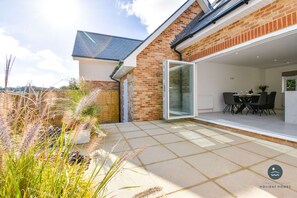 A modern house with a brick exterior, a glass door leading to a patio, and a table with chairs outside.