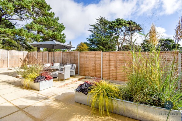 A patio area with outdoor furniture, planters with various plants, and a wooden fence. - Days Away - Luxury holiday home (Weymouth)