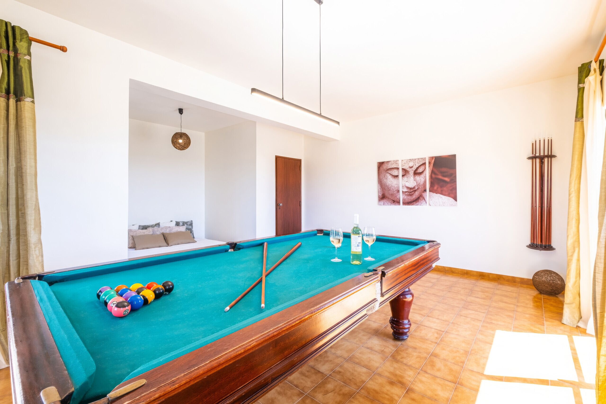 A pool table with billiard balls, a cue stick, and glasses of white wine.