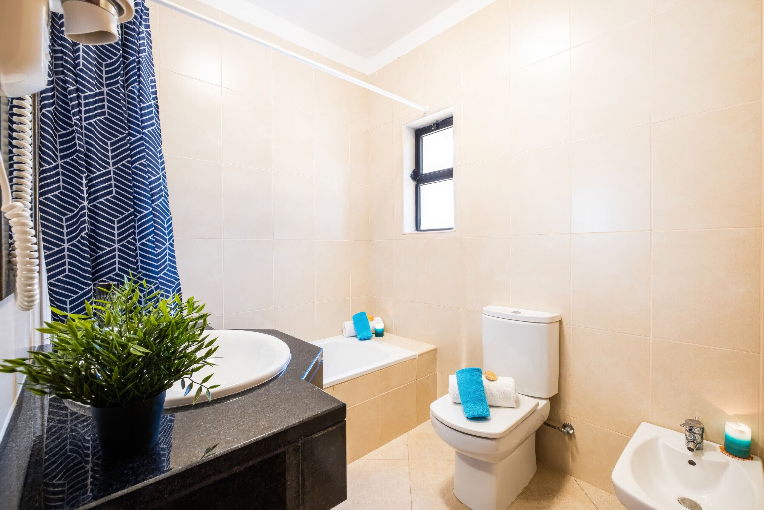 A modern bathroom with a sink, toilet, bidet, and a window.