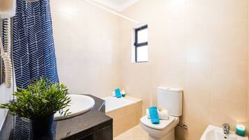 A modern bathroom with a sink, toilet, bidet, and a window.