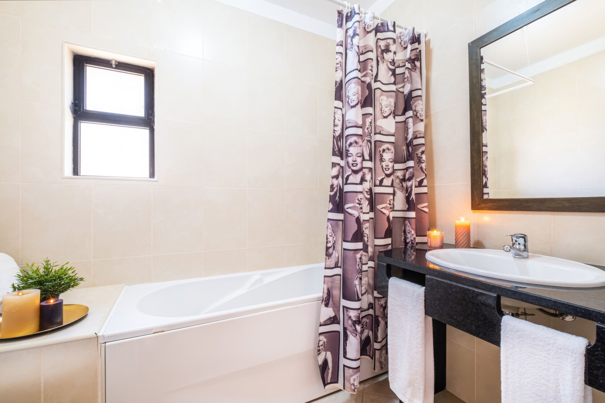 Un baño con bañera, lavamanos, espejo y cortina de ducha estampada.