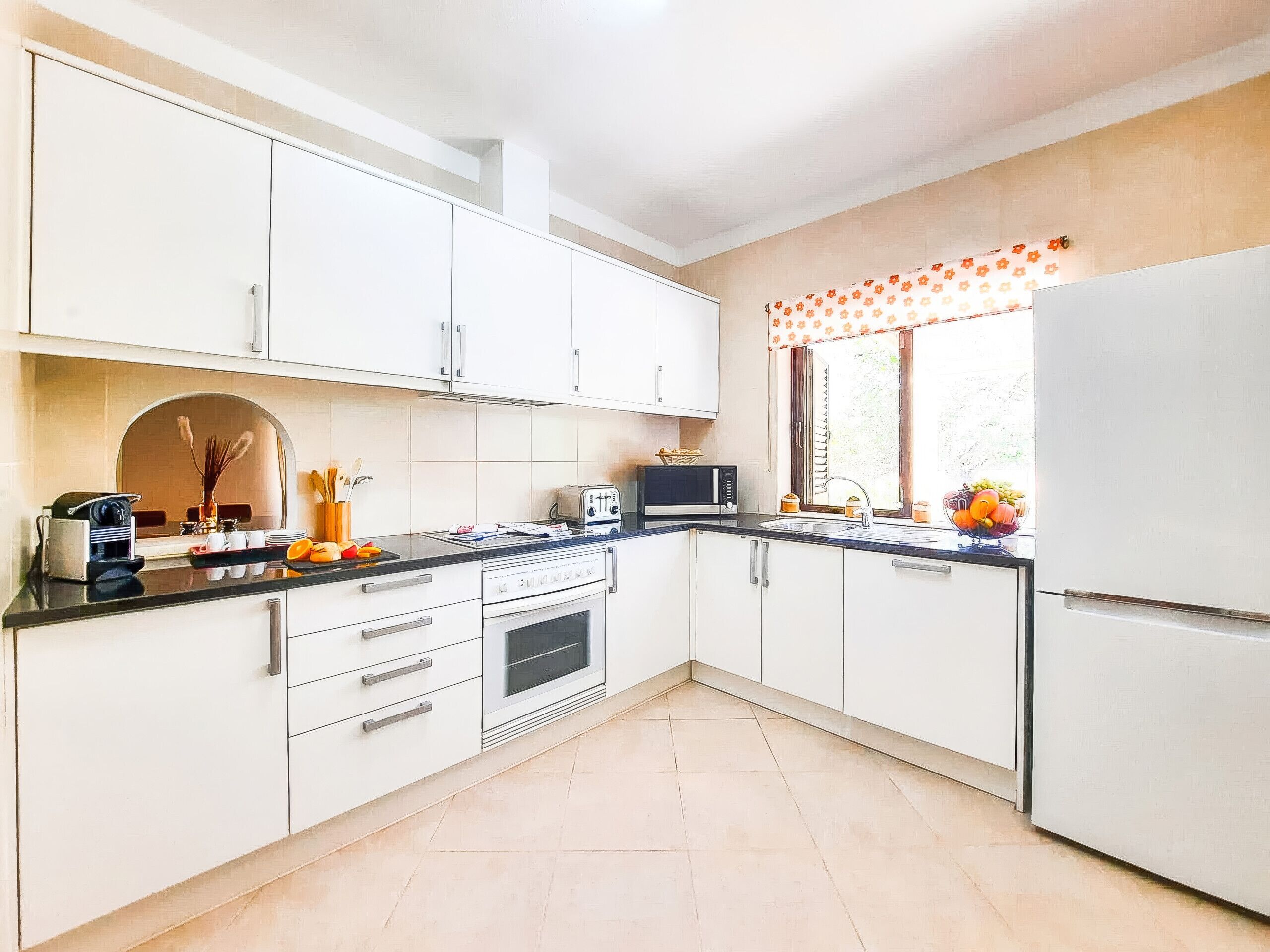 Una cocina con gabinetes blancos, encimera negra, microondas, tostadora y refrigerador.