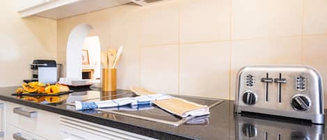 A modern kitchen with a built-in toaster, a stove with multiple controls, and a countertop with a cutting board, utensils, and a plate of fruit.