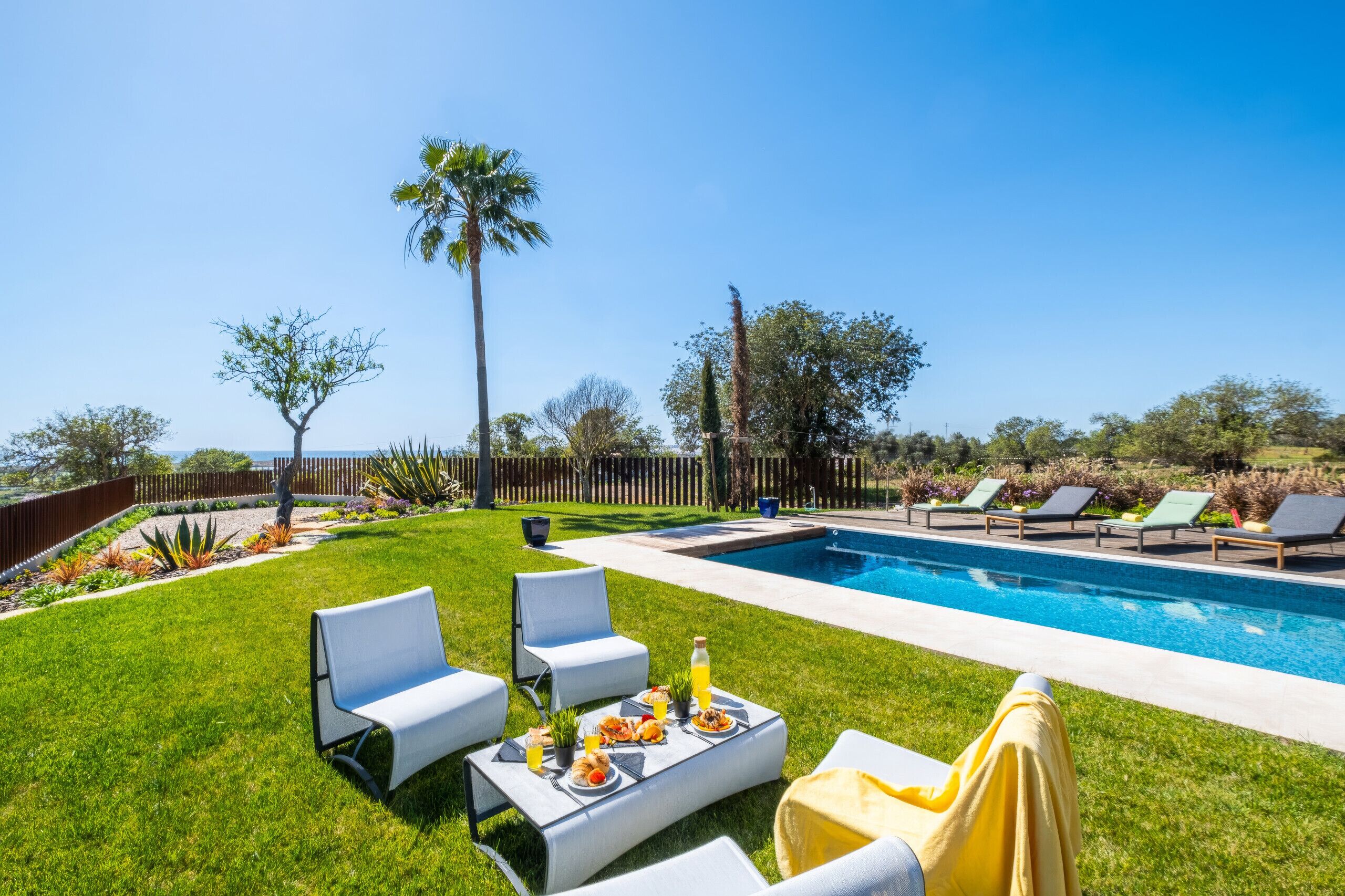 A backyard with a swimming pool, lounge chairs, and a dining table set for a meal.