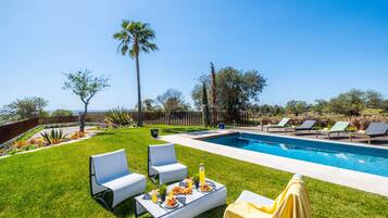 A backyard with a swimming pool, lounge chairs, and a dining table set for a meal.