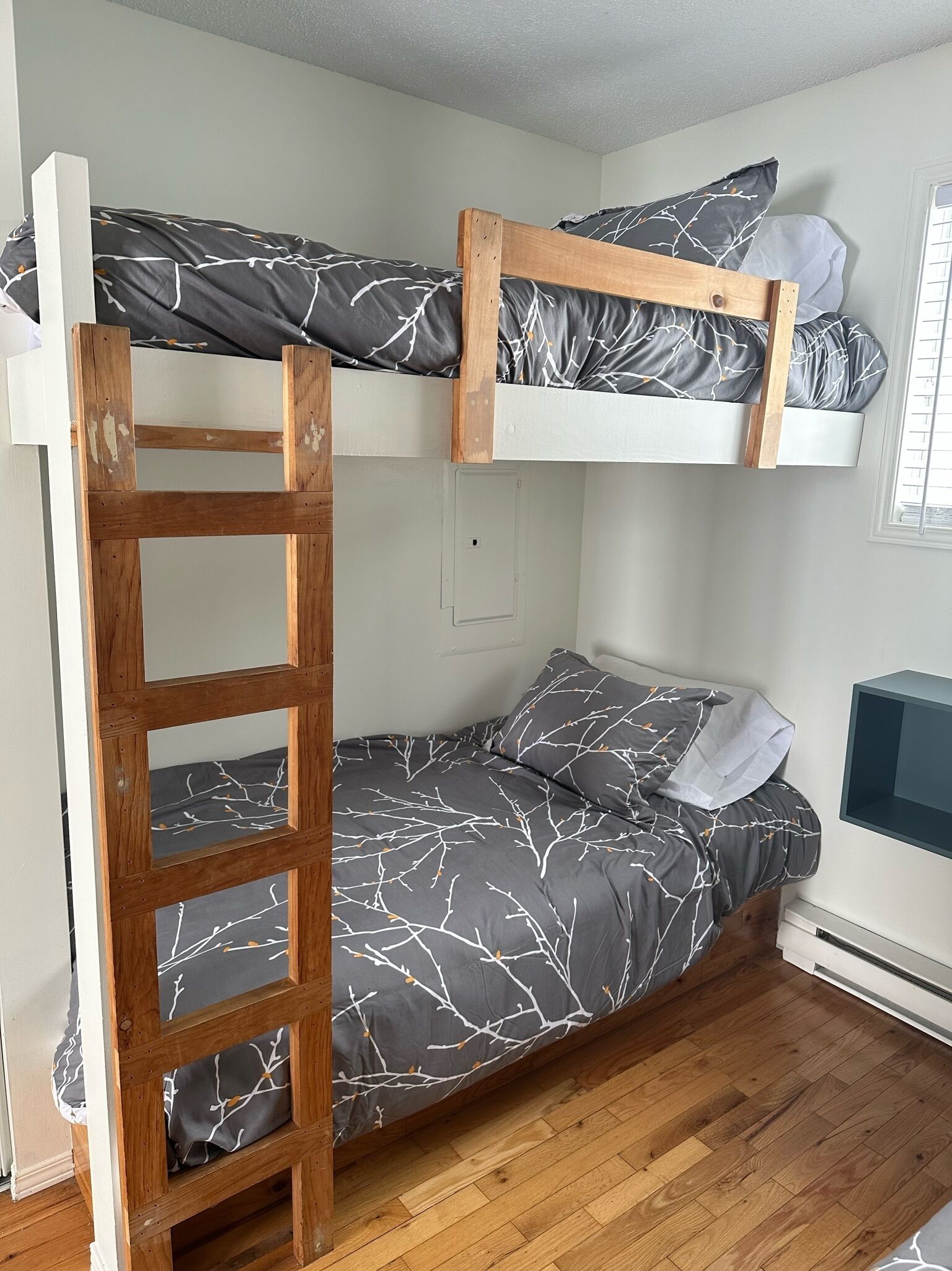A bunk bed with a wooden ladder, grey bedding with a branch pattern, and a television on the right.