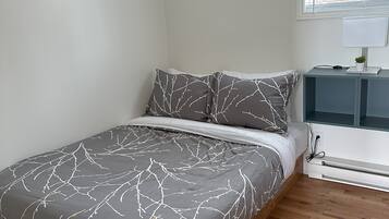 Een slaapkamer met een bed, nachtkastje, lamp en raam.