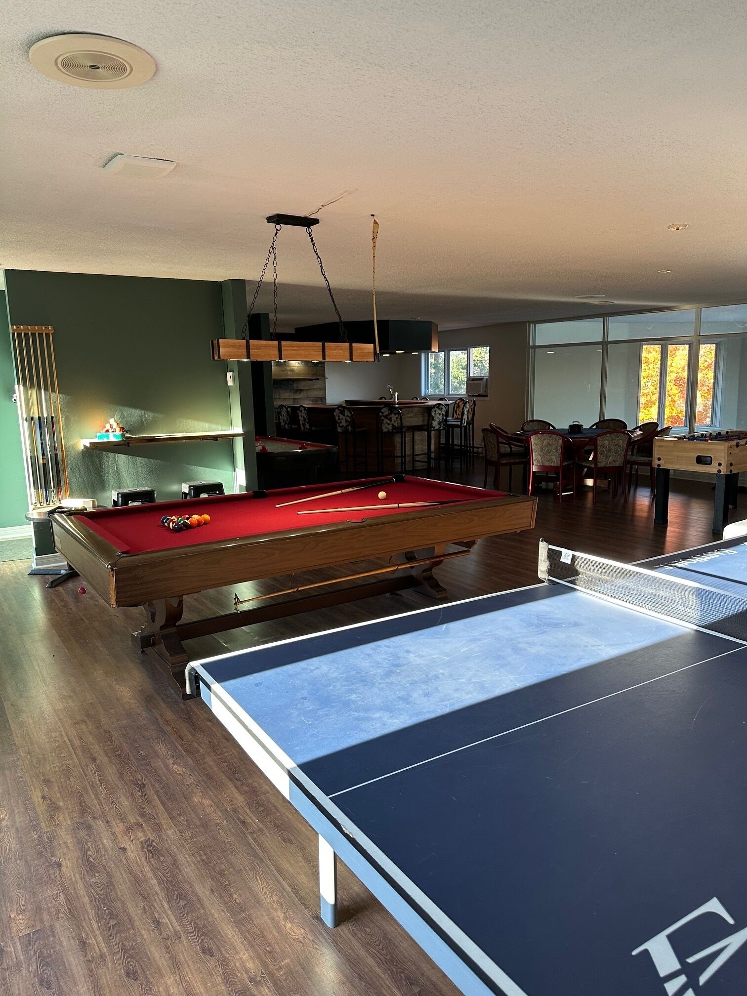 Una mesa de billar con superficie de fieltro rojo, una mesa de futbolín y una mesa de ping pong.