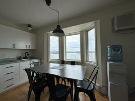 A kitchen with a dining table and chairs, a water dispenser, and a view of a lake through large windows.