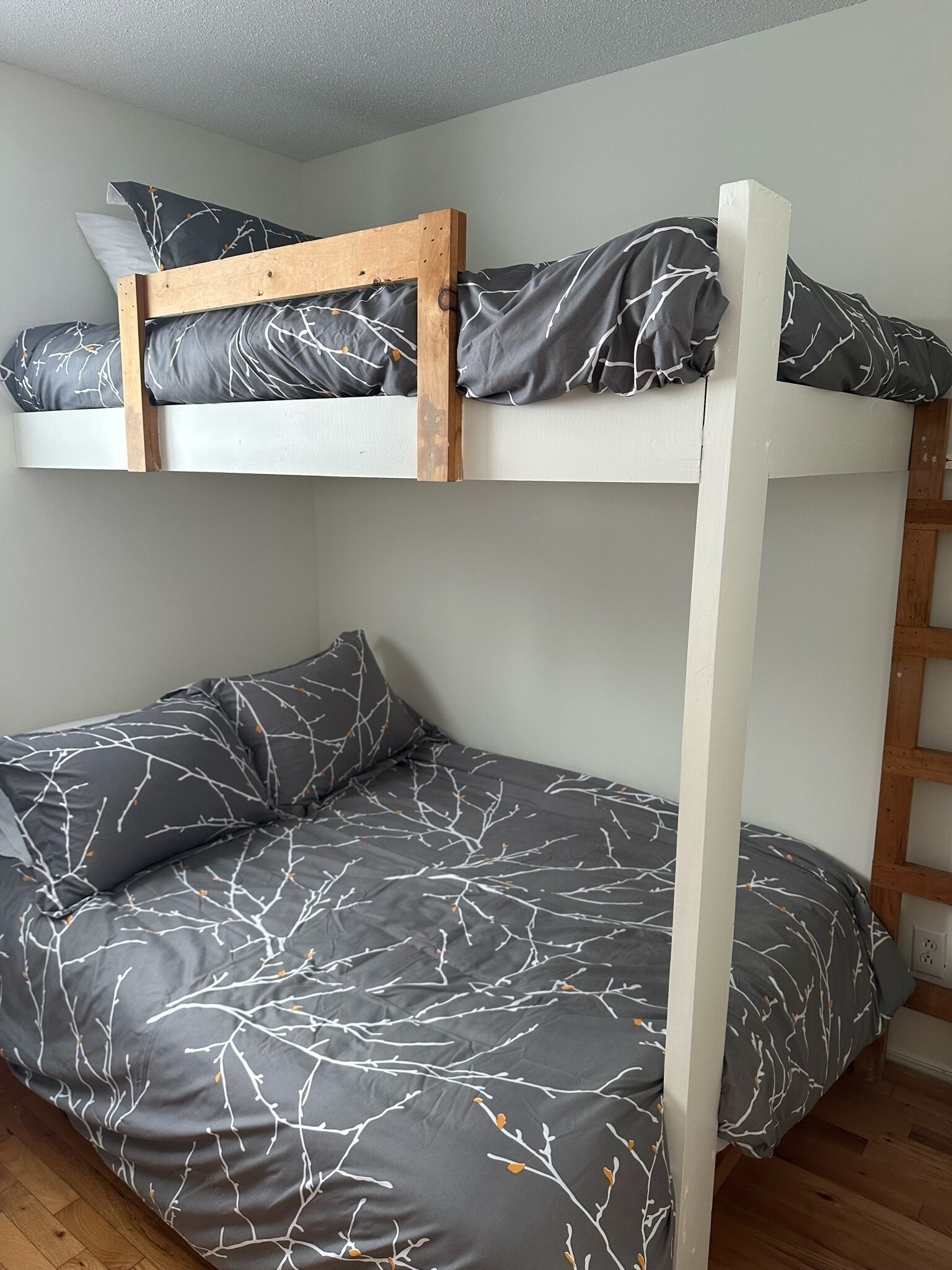 A bunk bed with a wooden frame and grey bedding with a branch pattern.