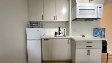 Cocina compacta con gabinetes blancos, microondas, tostadora, lavabo y dispensador de agua.