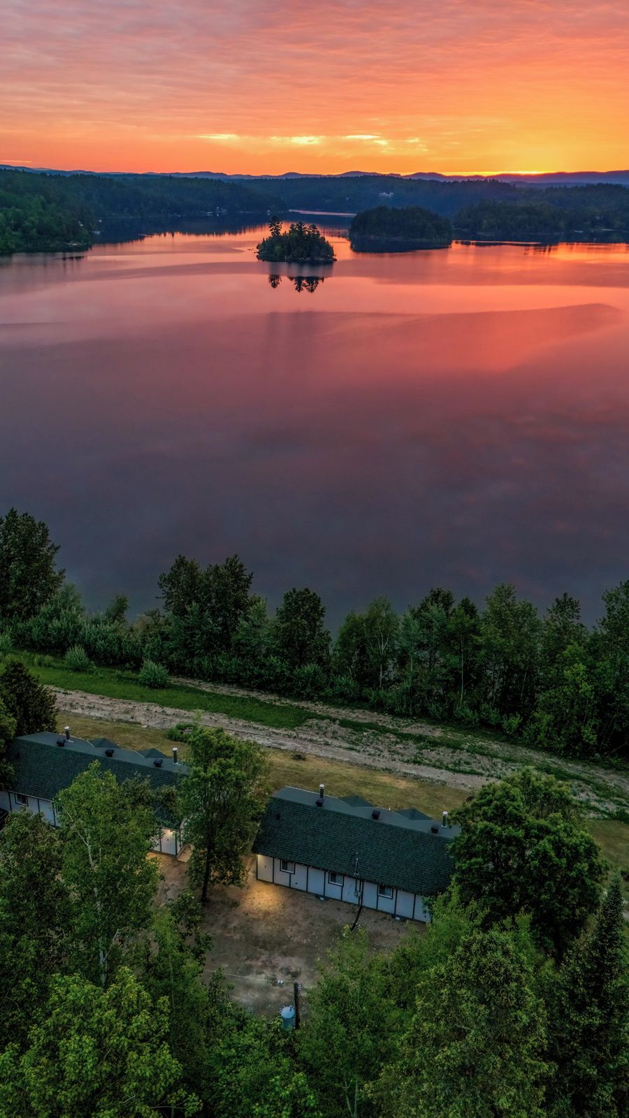 Une propriété au bord du lac, avec une petite île, entourée d’une forêt dense et offrant une vue dégagée sur le lac.